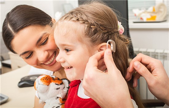 Smiling girl receiving hearing aid with woman and tiger doll