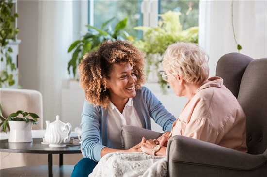 Woman smiling at and holding hands with seated older woman