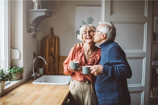 Couple embrace in kitchen holding coffee