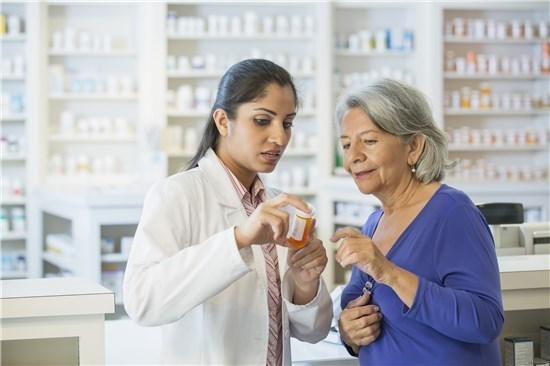 Pharmacist and woman look at prescription bottle in pharmacy